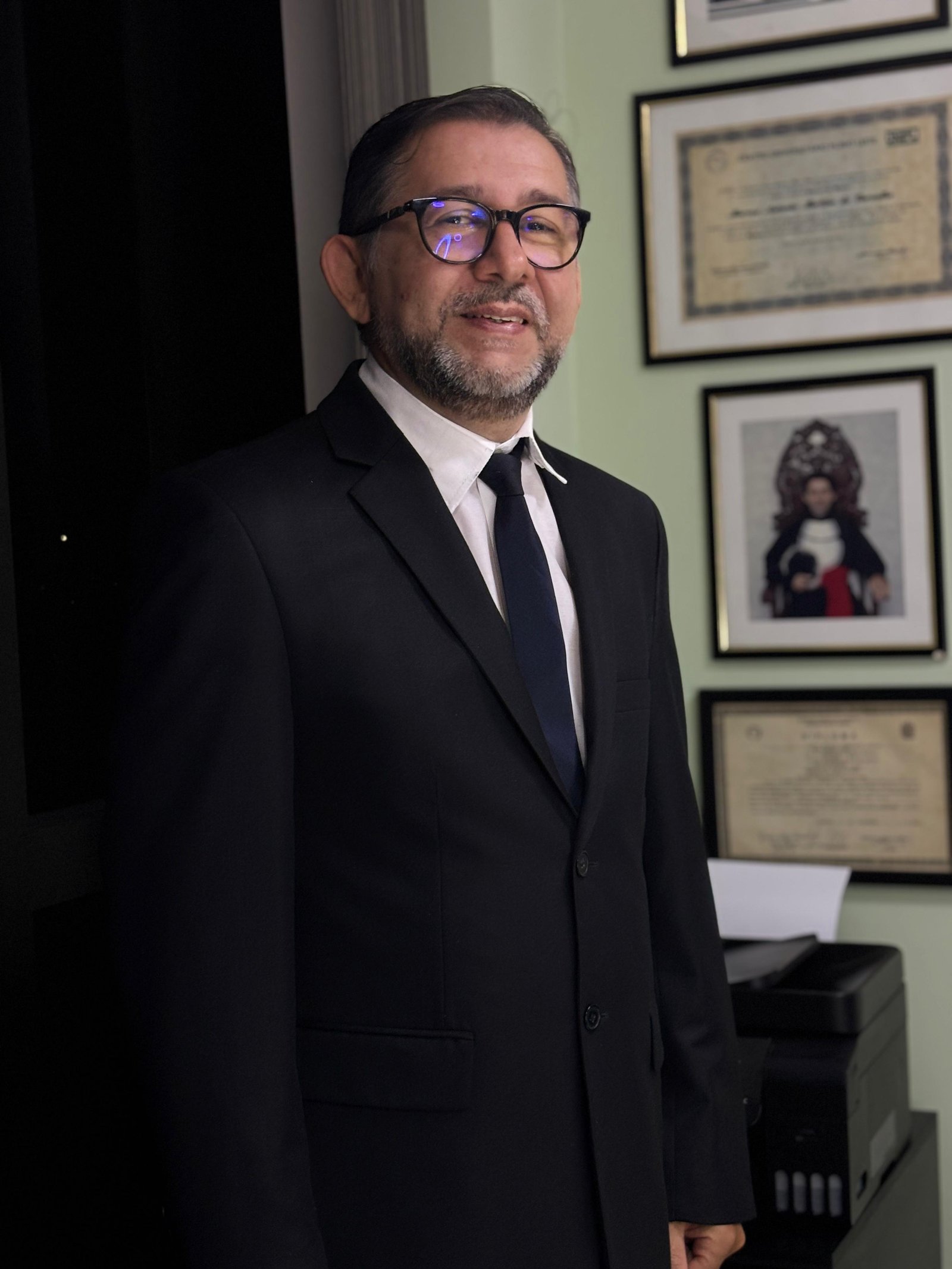 Retrato de Marcos Carvalho em seu escritório, em frente aos diplomas emoldurados.